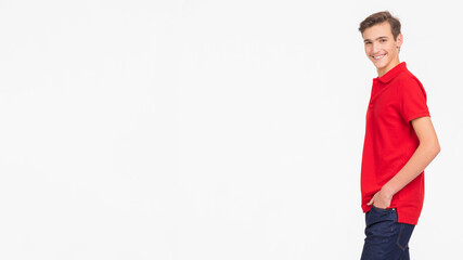 Fototapeta premium Photo of full length portrait of young happy smiling man isolated on a white background. Portrait of smiling handsome guy posing at studio. Attractive teenage boy in a red shirt and dark blue jeans