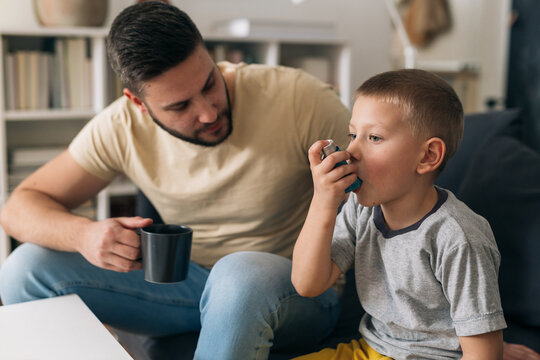 boy using asthma pump. father is sitting beside him