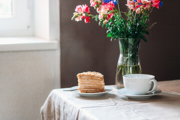 Obraz na płótnie Canvas Fresh honey cake on a plate with flowers in vase 