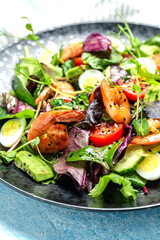Green salad with cherry tomatoes, cucumber, avocado, eggs and smoked shrimps, mixed greens. Healthy food. Clean eating. Food recipe background. Close up