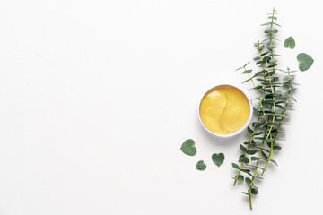 Cosmetic gold eye patches in box on white background with eucalyptus branches. Cosmetology background. Natural skin care concept
