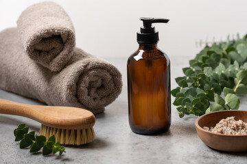 Spa body care. Transparent glass bottle with dispenser, body scrub in wooden bowl, natural massage brush and eucalyptus branches. Side view, close up view