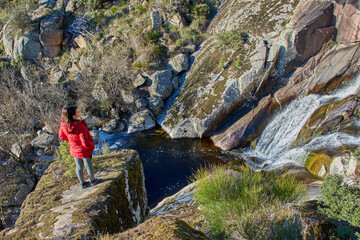 Girl in red jacket perched on a rock watching the waterfall and the natural scenery