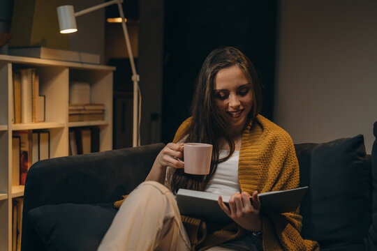 woman relaxing on sofa and reading book. evening moody ambience. she is enjoying time during weekend