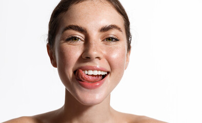 Beauty face of girl showing perfect white healthy smile, smiling with sticked tongue. Woman with glowing hydrated clean facial skin, thick eyebrows, nude makeup and naked shoulders, white background