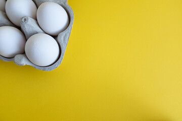 White eggs in an open egg carton on yellow background. Top view.