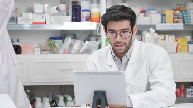 Middle eastern male pharmacist sits with customer and discusses choice of medication viewing from live steaming with digital tablet, online counseling, video call, medical technology, New Normal