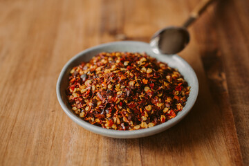 Red chili flakes in a bowl on wooden background. Red cayenne pepper.	
