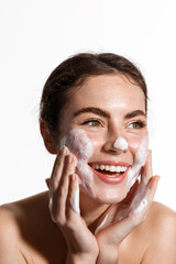 Portrait of cheerful laughing woman applying cleansing foam for washing face. Lovely brunette with attractive appearance. Skincare spa relax concept. Isolated on white background