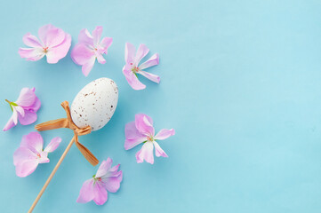 white Easter egg with a bow on a stick and red flowers on a blue background, easter background.