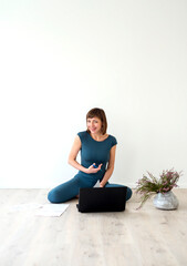 Fototapeta premium Woman sitting on floor next to laptop and working