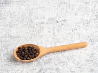 Spice black pepper in wooden spoon on a white concrete background