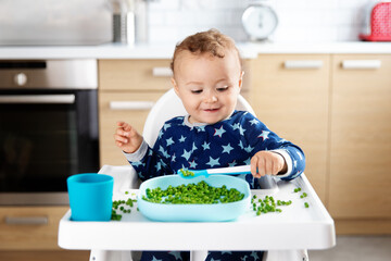 Smiling baby eating grean peas with spoon