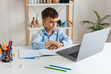 Clever kid doing homework using laptop and internet. Elementary school e-learning via video call. Boy studying online at home