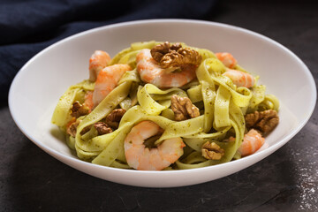 A view of a plate of Tagliatelle pasta with shrimp, pesto sauce, walnut on dark table. Italian food. Mediterranean cuisine.