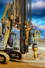 Hydraulic drilling rig against the blue cloudy sky. Vertical image. Installation of bored piles by drilling. Foundations and foundations. Drilling in the ground.