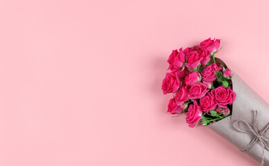 Bouquet of small flowered roses wrapped in craft paper on pink background with copy space.