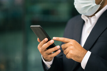 Young businessman wearing protection mask using smartphone in downtown urban city. Asian man in suit walking in the city.