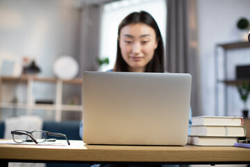 Blur background of young asian woman sitting at desk and surfing internet on portable computer. Focus on wireless laptop. Concept of freelance and technology.