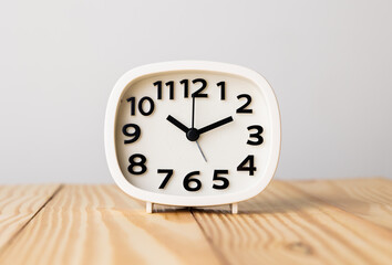 Small white alarm clock, black numbers, set the time for 10.10 o'clock, placed on a wood table.