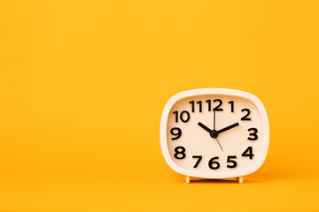 Fototapeta na wymiar Small white alarm clock, black numbers, set the time placed on a table. Clock on isolated yellow background.
