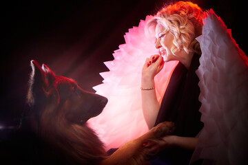Blonde woman with white angel wings and a large German shepherd dog. Photo shoot in studio