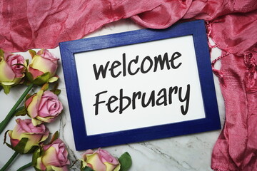 Welcome February written on blue frame with rose flower flat lay on marble background