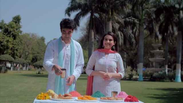 A man offering a glass of Thandai on Holi festival - Indian festival. Cheerful youngsters celebrating the Indian festival of colors outdoors in the park