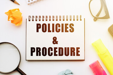 Text POLICIES&PROCEDURE in notebook on white table with office tools.