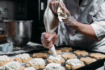 Chefs hands with pastry bag squeezing out cream dough for baking 