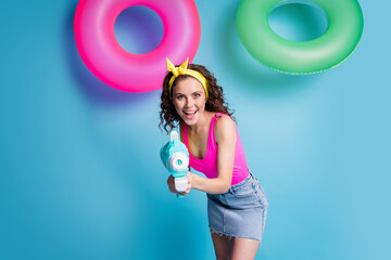 Photo of young excited girl happy positive smile play game shoot water pistol isolated over blue...