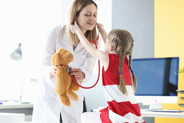 Little girl putting stethoscope on to doctor pediatrician in clinic