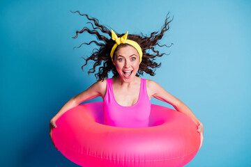 Photo of young excited girl blow hair happy positive smile hold pink float ring ready swim isolated over blue color background