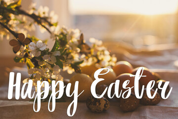 Happy Easter text on modern pastel easter eggs with cherry blossoms on rustic table in sunset light, handwritten sign. Beautiful stylish greeting card. Seasons greetings © sonyachny
