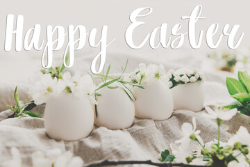 Happy Easter text on natural eggs in cute floral wreaths on linen fabric with cherry blossoms and white petals in soft light, handwritten sign. Beautiful stylish greeting card. Seasons greetings © sonyachny