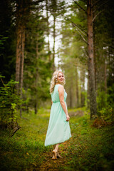 Young beautiful blonde in a light green dress posing in the woods in summer, selective focus