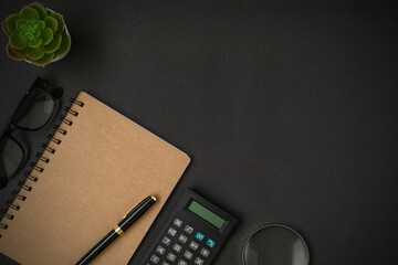 Black vintage alarm clock, calculator, spectacles, notebook and a pen with a copy space on black background. Flat lay.