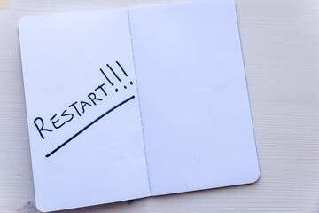 Restart! Starting again after a break, after a pandemic. Word "Restart" written in black ink on a blank page of a notebook, placed on a wooden surface. 