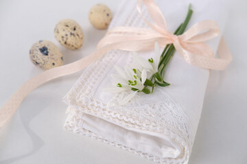 Obraz na płótnie Canvas white linen napkin, trimmed with handmade lace, delicate snowdrop flower, three quail eggs lie on light table, concept of luxury serving spring breakfast, diet, Easter holiday