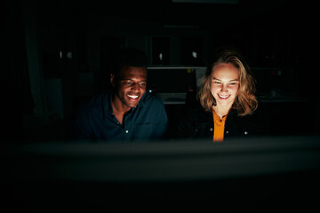 Two happy diverse business people sitting together working till late night in dark office