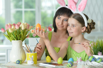 happy mother with daughter wearing rabbit ears decorating  Easter eggs