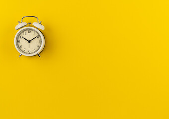 A white retro alarm clock shows ten hours and ten minutes on a yellow paper background with a copy space. Flat lay. Top view. Place for text. The concept of summer, sunny and happy time. Time: 10.10