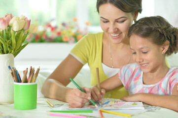 little cute girl with mother drawing at the table at home