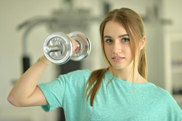 Sporty young woman training with dumbbells in gym