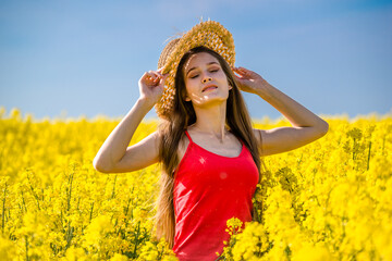Naklejka na ściany i meble Beautiful young woman portrait in rapeseed field. Rural scene with girl enjoying sun in yellow blooming field. Concept of joy, happiness and freedom.