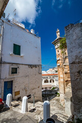 Sculpture on roof. Art in Puglia, Italy under the clear blue sky of a sunny summer day, travel photography, street view of narrow pedestrian street covered by stone tiles. No people in the frame