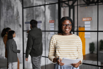 Obraz na płótnie Canvas Waist up portrait of young African-American businesswoman standing by glass wall while planning project in modern office, copy space