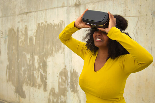 Fototapeta African american woman with afro hair and yellow t-shirt playing with virtual goggles.