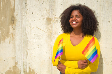 African american woman with afro hair wearing yellow t-shirt and gay pride flags.