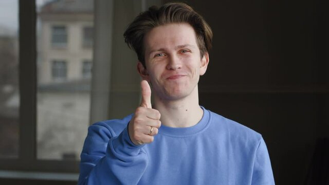 Portrait of young caucasian guy millennial male model teen wears blue sweatshirt standing alone, posing makes gesture hey you, showing index finger looking at camera, raises thumb up, symbol of agree